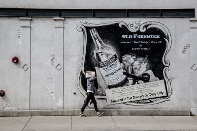 person walking on sidewalk in front of wall wih advertisement