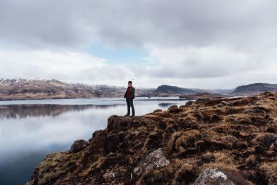 man standing near water and mountains