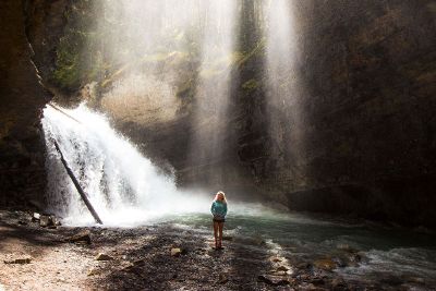 woman infront water fall and sun rays through trees
