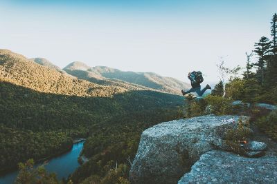 hiker leaping on cliff over mountains