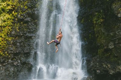 man swinging on rope over waterfall