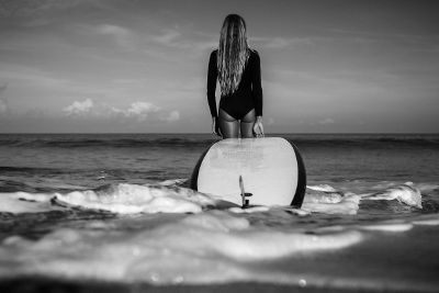 woman carrying surfboard into water